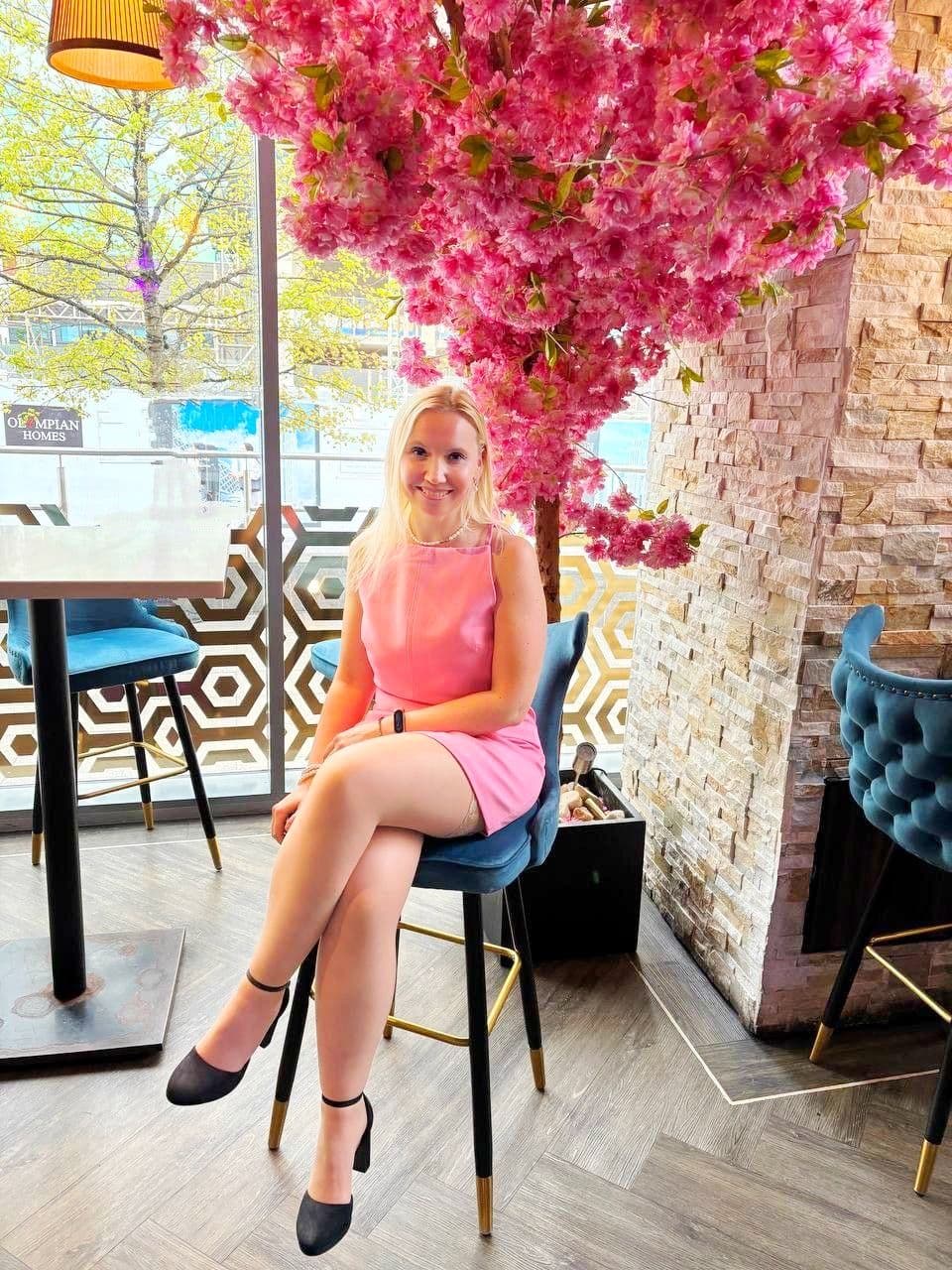 Anastasiia in a pink dress sitting beneath a pink blossom display in a café